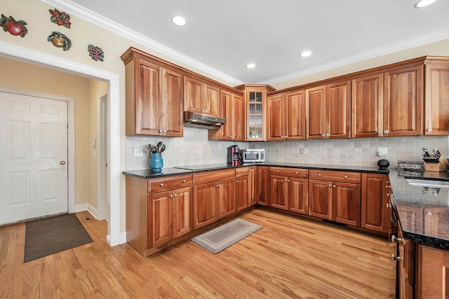 kitchen with dark stone counters, ornamental molding, light hardwood / wood-style flooring, and tasteful backsplash