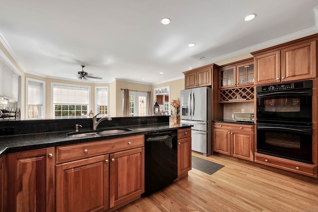 kitchen with sink, ornamental molding, light hardwood / wood-style flooring, black appliances, and dark stone countertops