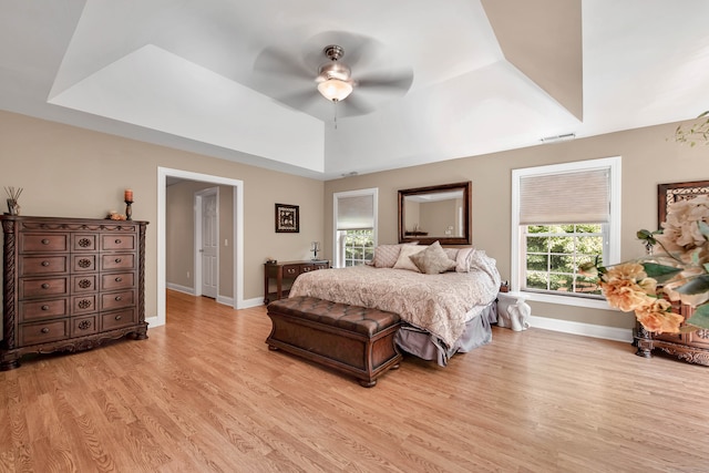 bedroom with a raised ceiling, light hardwood / wood-style floors, and ceiling fan