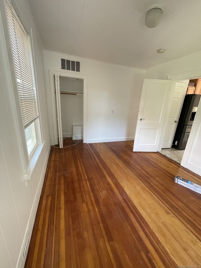 unfurnished bedroom featuring black refrigerator, multiple windows, and hardwood / wood-style flooring