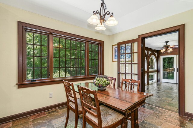 dining room with dark tile patterned floors, a healthy amount of sunlight, and ceiling fan with notable chandelier