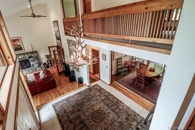 interior space featuring ceiling fan with notable chandelier, hardwood / wood-style flooring, a stone fireplace, and high vaulted ceiling