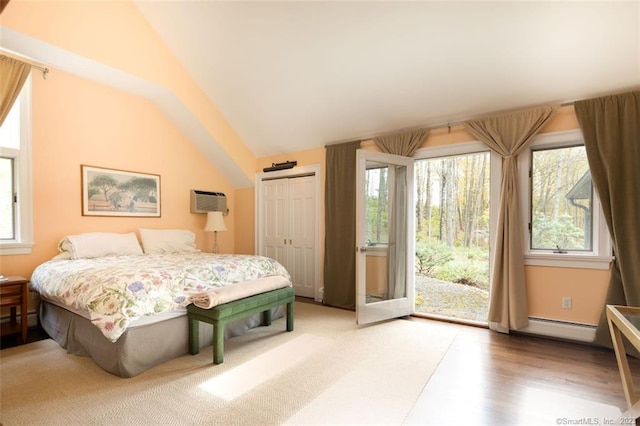 bedroom with a closet, wood-type flooring, a baseboard heating unit, high vaulted ceiling, and access to exterior