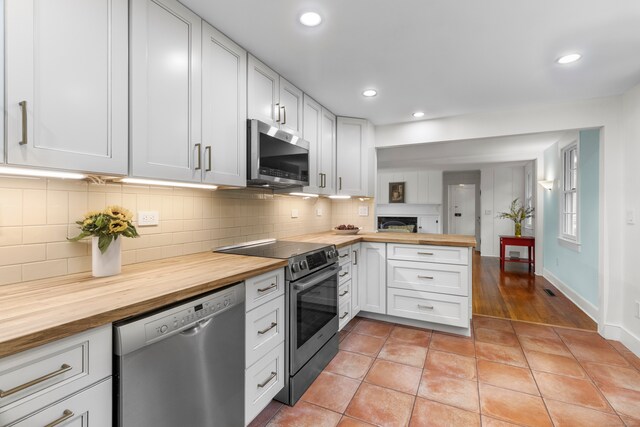 kitchen with wooden counters, tasteful backsplash, white cabinets, appliances with stainless steel finishes, and light tile patterned floors