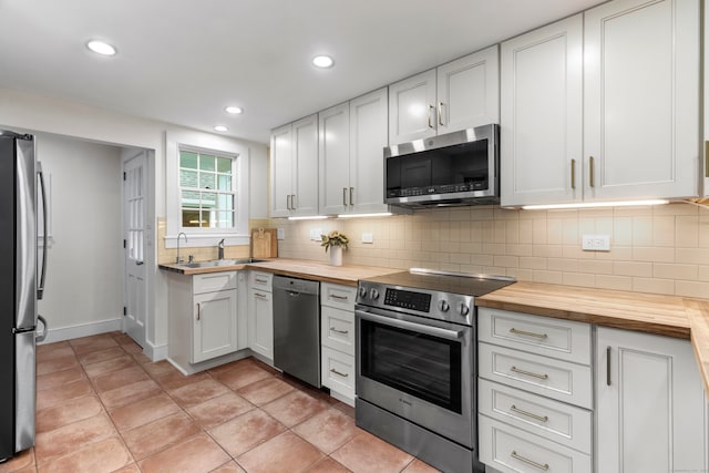 kitchen with stainless steel appliances, white cabinets, sink, butcher block countertops, and backsplash