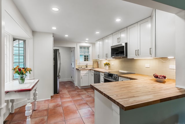 kitchen featuring kitchen peninsula, wooden counters, stainless steel appliances, and white cabinets