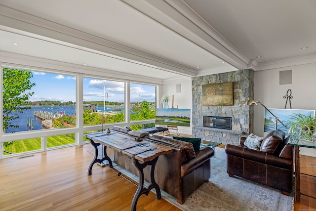 living room featuring a stone fireplace, light hardwood / wood-style flooring, a water view, and ornamental molding