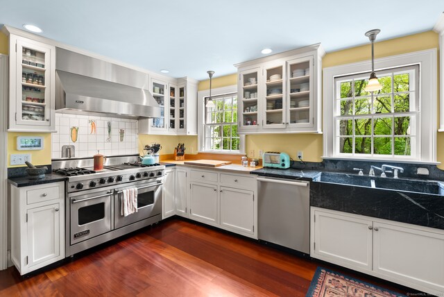 kitchen with hanging light fixtures, wall chimney exhaust hood, white cabinetry, and appliances with stainless steel finishes