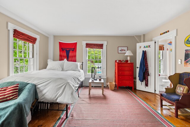 bedroom with hardwood / wood-style floors, connected bathroom, radiator, and multiple windows