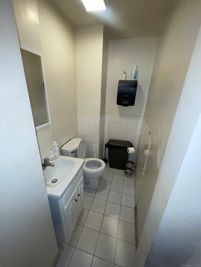 bathroom featuring tile flooring, vanity, toilet, and tile walls