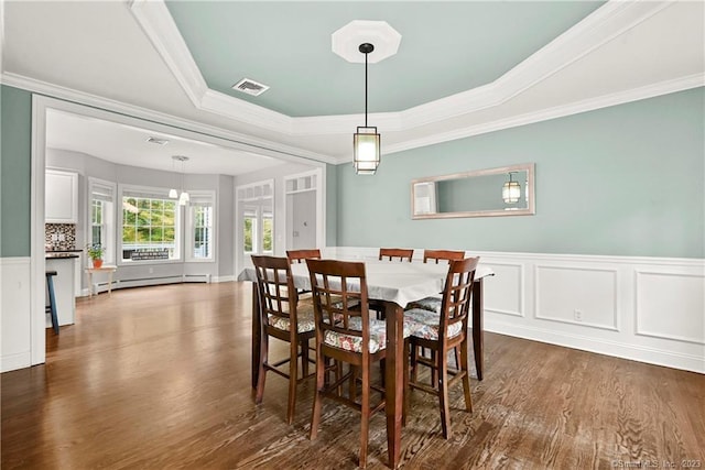 dining room with dark wood-type flooring, a baseboard heating unit, a tray ceiling, and ornamental molding