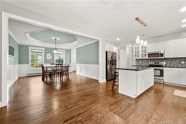 kitchen featuring pendant lighting, appliances with stainless steel finishes, white cabinetry, a raised ceiling, and a breakfast bar