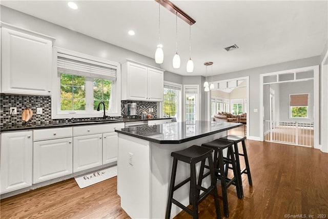 kitchen with hanging light fixtures, sink, white cabinetry, a kitchen island, and a breakfast bar area