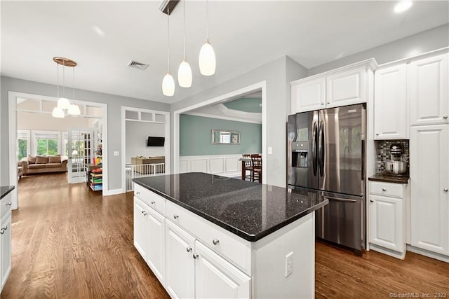 kitchen with stainless steel fridge, decorative light fixtures, white cabinets, dark stone counters, and a center island