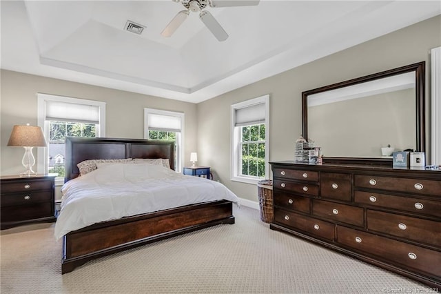 bedroom featuring ceiling fan, multiple windows, a tray ceiling, and light carpet