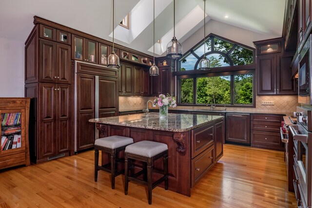 kitchen with high end appliances, an island with sink, dark brown cabinetry, and dark stone countertops