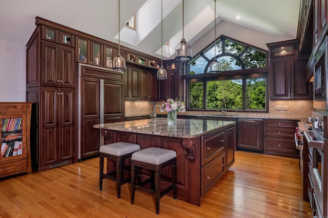 kitchen featuring tasteful backsplash, dark stone countertops, dark brown cabinets, and a center island with sink