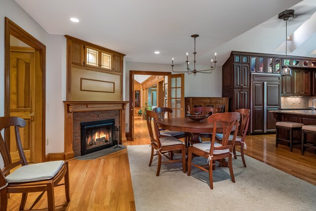 dining space with a brick fireplace, an inviting chandelier, and light hardwood / wood-style floors