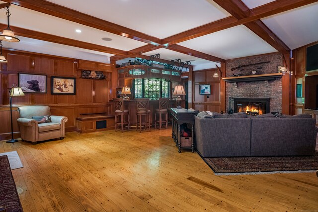 living room with light wood-type flooring, beam ceiling, wooden walls, a fireplace, and indoor bar