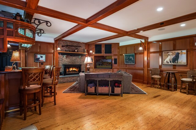 living room with beamed ceiling, wooden walls, a fireplace, and light hardwood / wood-style floors