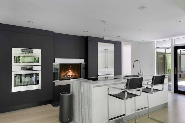 kitchen with light wood-type flooring, a wall of windows, double oven, and a spacious island