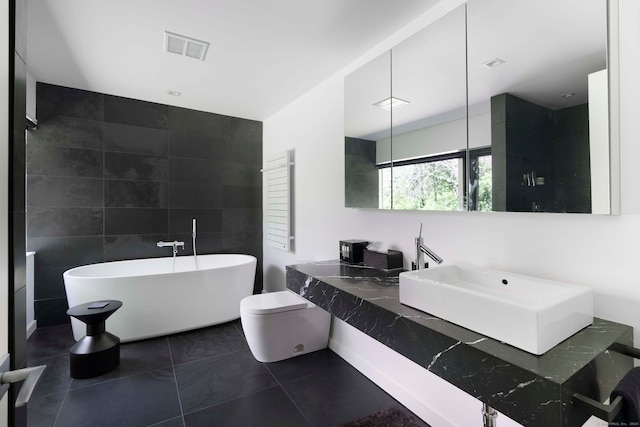 bathroom featuring tile walls, a bathing tub, vanity, tile patterned flooring, and toilet