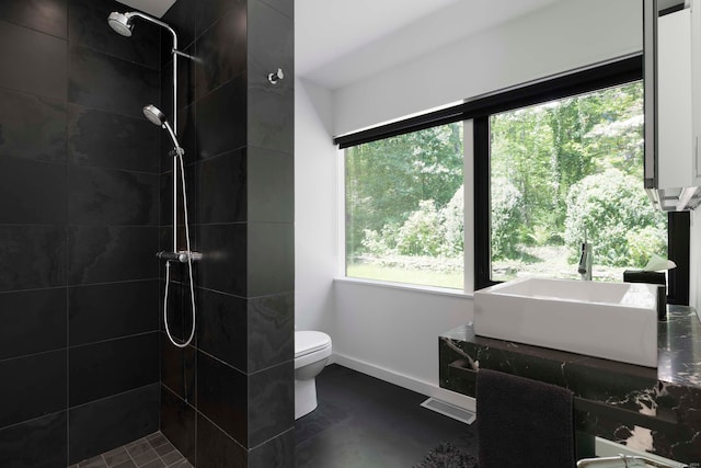 bathroom with tiled shower, toilet, and sink