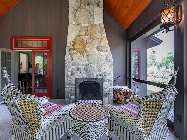 living room with wood walls, high vaulted ceiling, wooden ceiling, and a stone fireplace