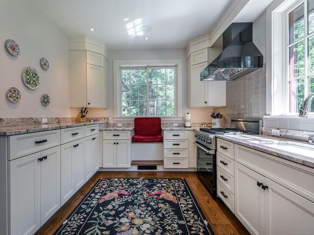 kitchen featuring stainless steel range, dark hardwood / wood-style flooring, light stone counters, decorative backsplash, and wall chimney exhaust hood