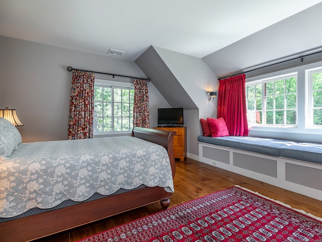 bedroom with multiple windows, hardwood / wood-style floors, and vaulted ceiling