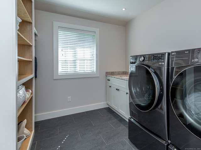 clothes washing area with dark tile patterned floors, washing machine and clothes dryer, and cabinets