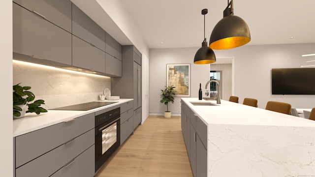 kitchen featuring backsplash, oven, hanging light fixtures, light wood-type flooring, and sink