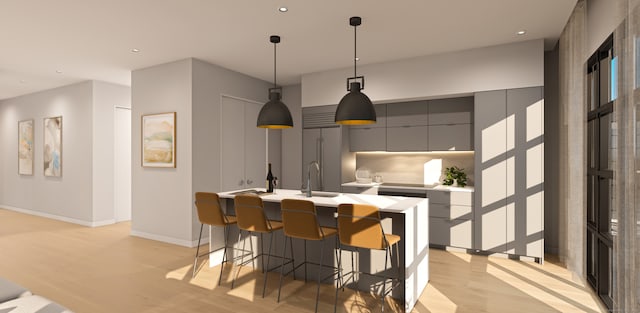 kitchen with light hardwood / wood-style floors, hanging light fixtures, a center island with sink, gray cabinetry, and a breakfast bar area