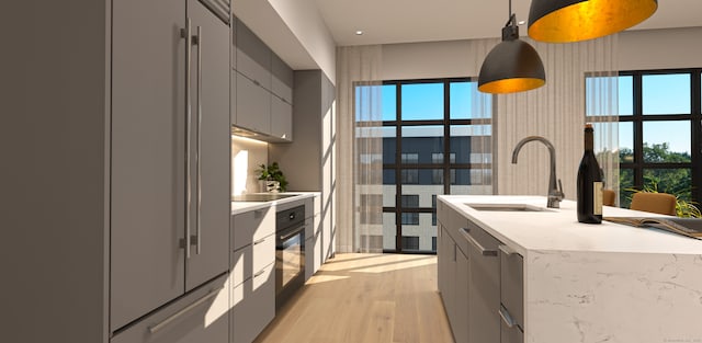 kitchen featuring gray cabinetry, light stone countertops, light wood-type flooring, sink, and pendant lighting