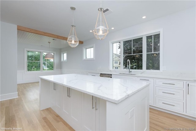 kitchen with sink, pendant lighting, beam ceiling, light hardwood / wood-style flooring, and a kitchen island