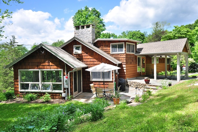 rear view of house with a yard, a patio, a shingled roof, and a chimney