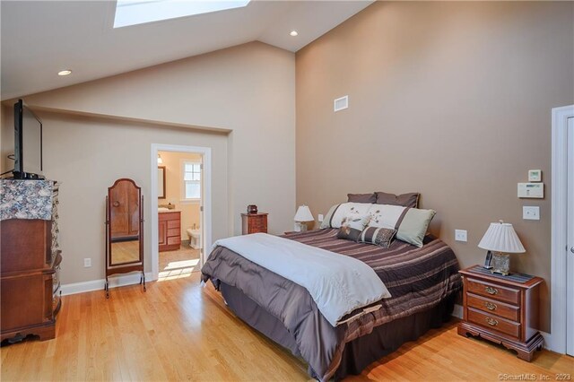 bedroom with a skylight, ensuite bathroom, high vaulted ceiling, and light wood-type flooring