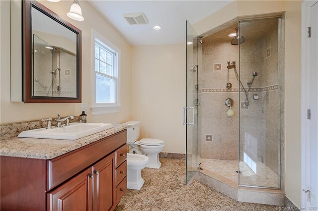 bathroom with vanity, a shower with door, toilet, and a bidet