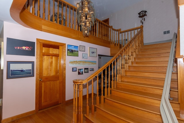 staircase featuring a high ceiling, an inviting chandelier, and wood-type flooring