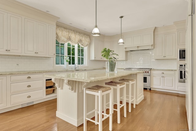 kitchen featuring a kitchen island, appliances with stainless steel finishes, decorative light fixtures, light stone countertops, and light wood-type flooring