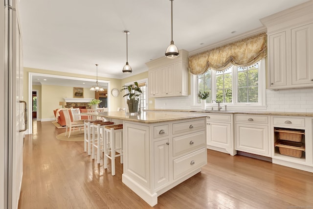 kitchen with a kitchen island, decorative light fixtures, white cabinetry, light stone counters, and light wood-type flooring