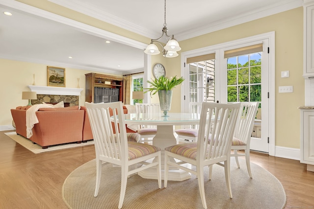 dining area featuring ornamental molding, a stone fireplace, a notable chandelier, and light hardwood / wood-style flooring