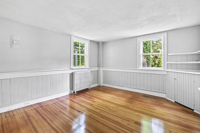 unfurnished room with hardwood / wood-style floors, radiator, and a wealth of natural light