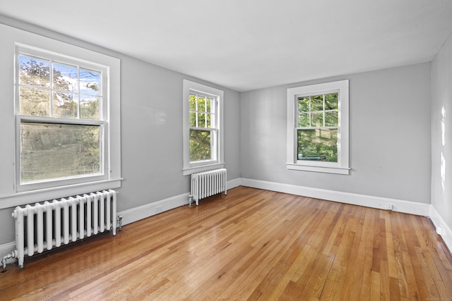 unfurnished room featuring radiator heating unit and light hardwood / wood-style flooring