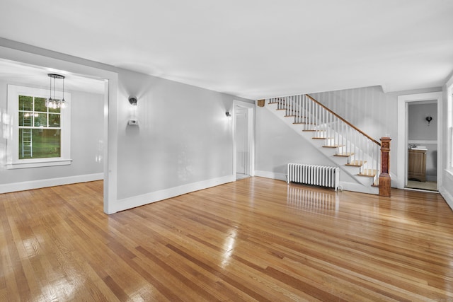 unfurnished living room with radiator heating unit, an inviting chandelier, and light hardwood / wood-style flooring