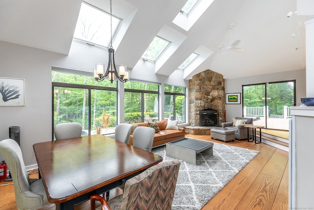 dining space with light hardwood / wood-style floors, ceiling fan with notable chandelier, high vaulted ceiling, a skylight, and a stone fireplace