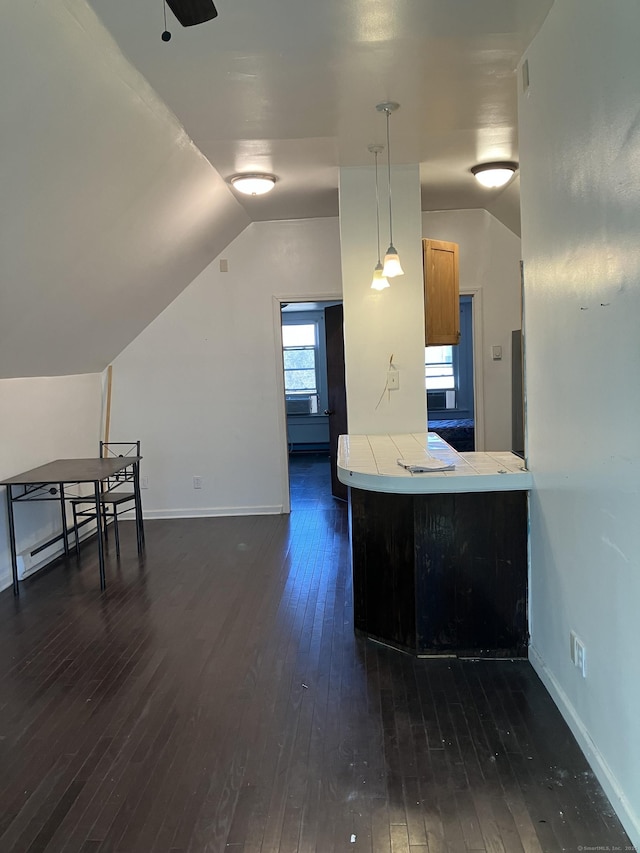 kitchen with dark wood-type flooring, kitchen peninsula, vaulted ceiling, and hanging light fixtures