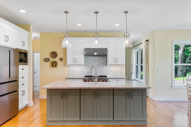 kitchen featuring light stone counters, a center island with sink, light hardwood / wood-style flooring, white cabinetry, and stainless steel refrigerator