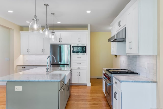 kitchen featuring appliances with stainless steel finishes, a center island with sink, white cabinets, light hardwood / wood-style floors, and hanging light fixtures