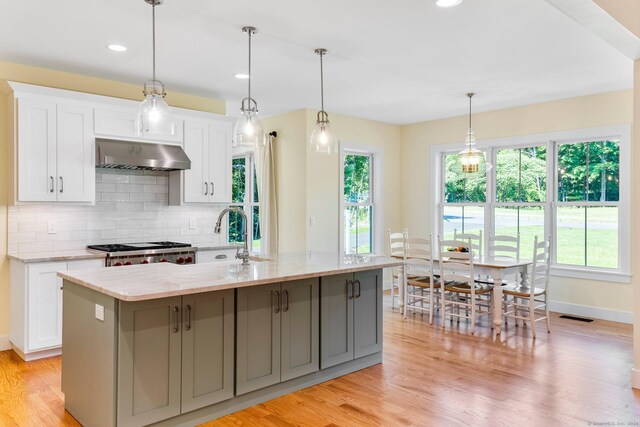 kitchen featuring light wood-type flooring, stainless steel range, exhaust hood, a center island with sink, and white cabinets